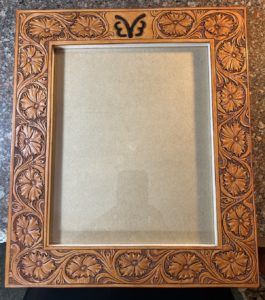 Carved leather picture frame with floral carving design and a brand.